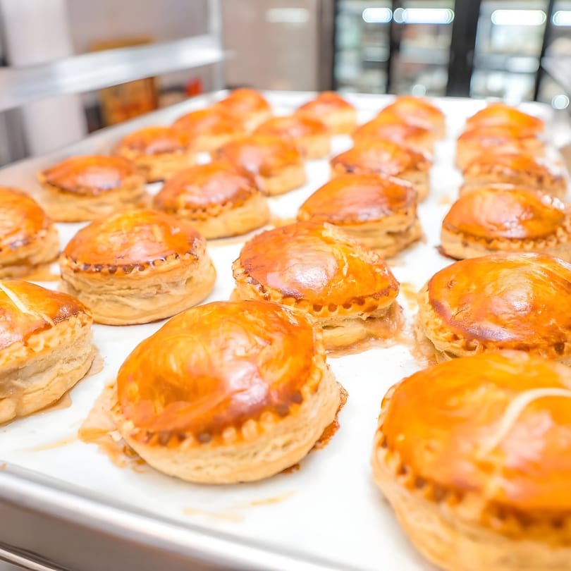 Rows of golden-brown Vietnamese pâté chaud pastries on a white baking sheet.