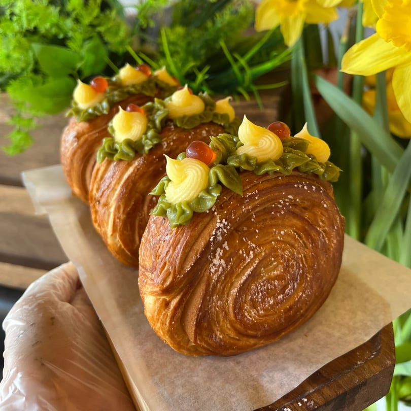 Three Paris Bánh Mì croissants with green and yellow frosting, and orange boba, on a wooden tray.