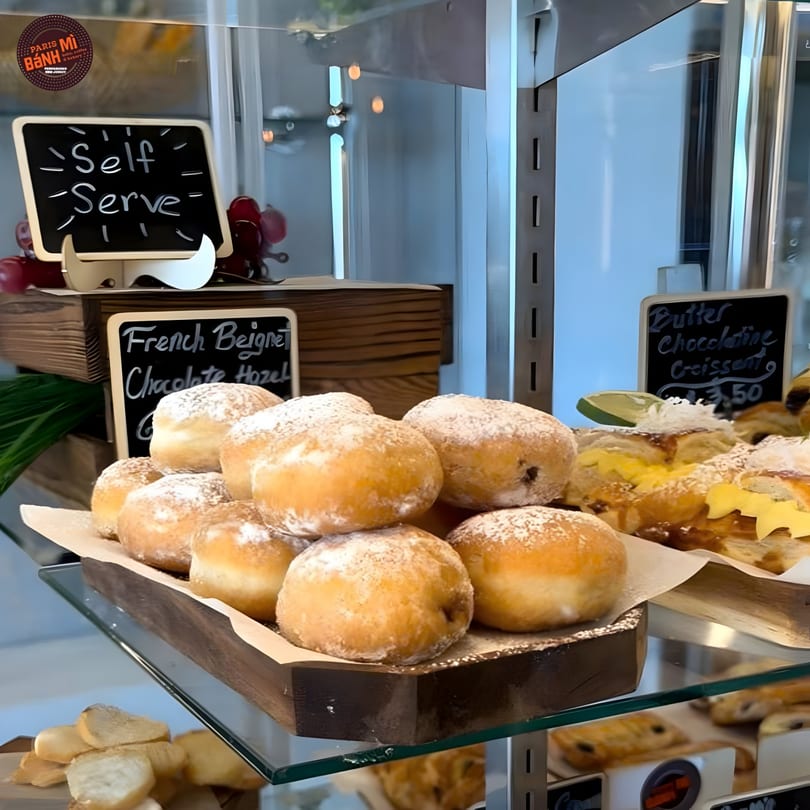 A display case at Paris Bánh Mì New Jersey filled with powdered sugar French beignets and croissants.