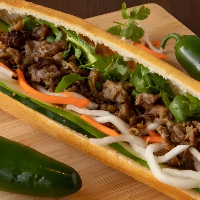 A Vietnamese Bánh Mì sandwich with meat, cilantro, pickled carrots, cucumbers, and jalapeños on a wooden board.
