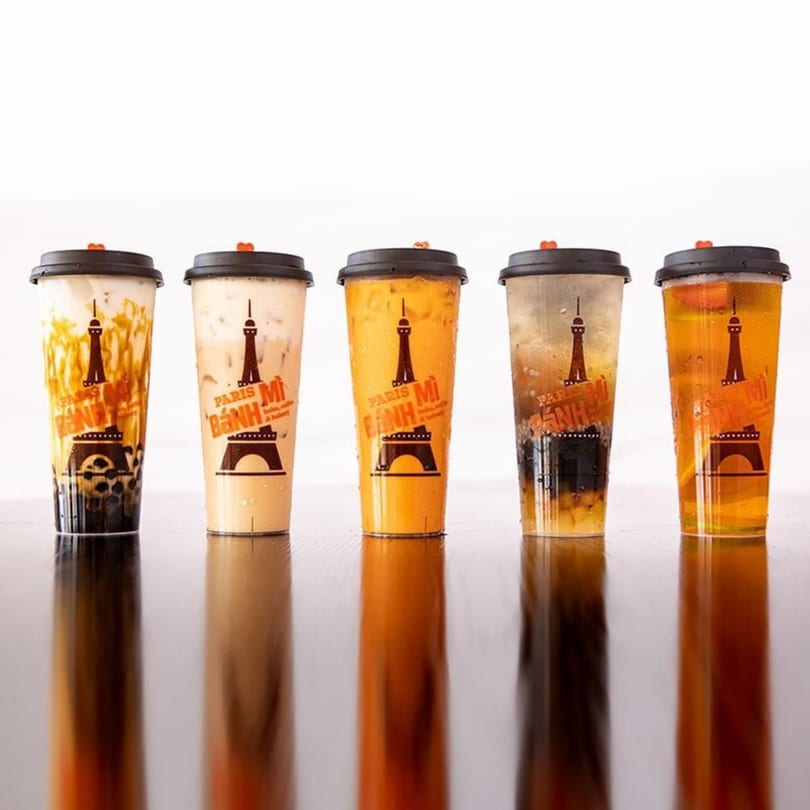 Five Paris Bánh Mì bubble tea drinks in clear cups with black lids on a reflective surface.