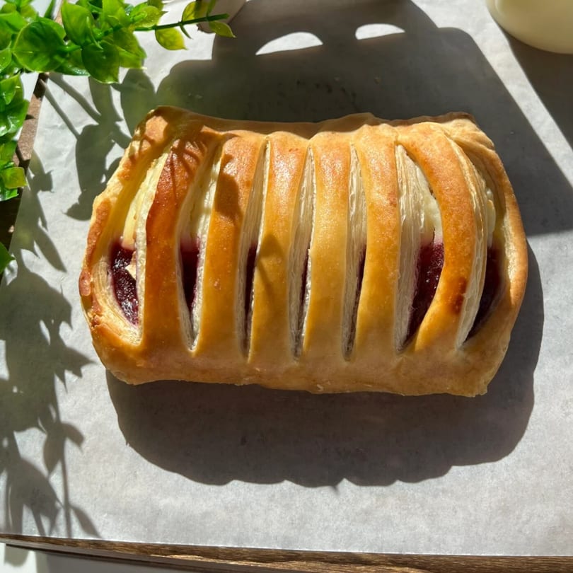 A golden-brown pastry with berry filling sits on white parchment paper, with green leaves in the background.